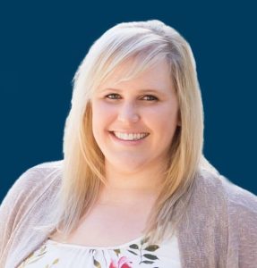 Kelly Wende smiling in front of a navy blue background.