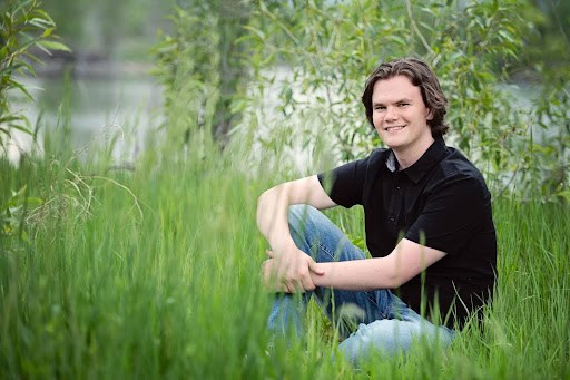 Ben Egan, Erie High School Graduate sitting in a grassy area with his knee up and smiling