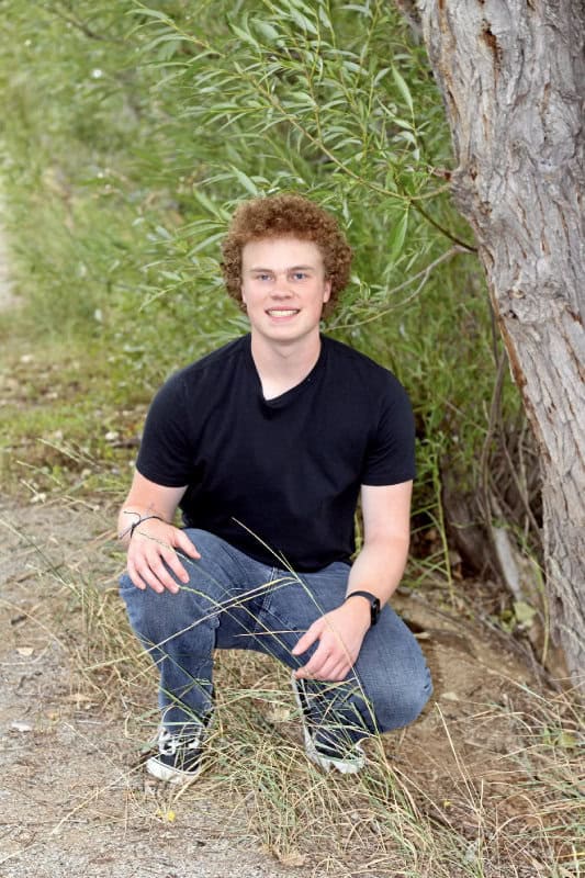 Isaac Campbell posing for senior photo in front of a tree. 