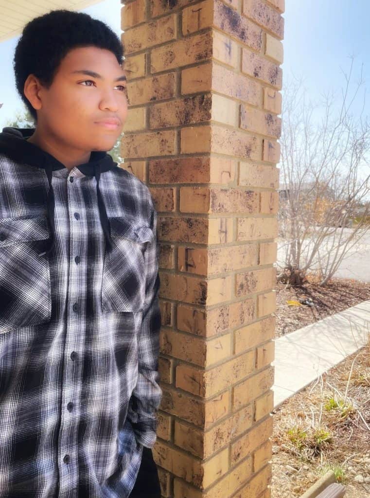 Male student, Derrek, leaning against brick column posing for senior photo.