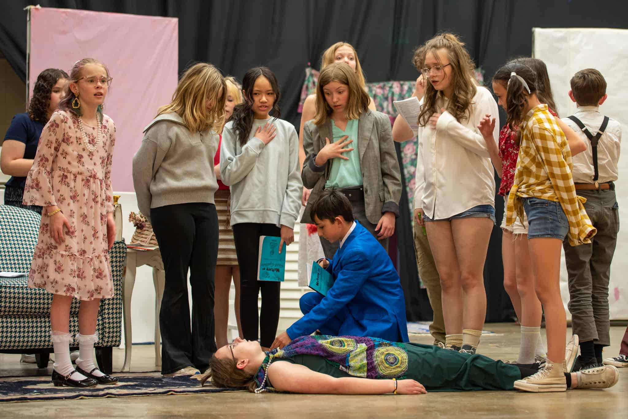 Una fila de alumnas sobre un alumno que toma el pulso a una alumna tumbada en el escenario durante una obra de teatro.