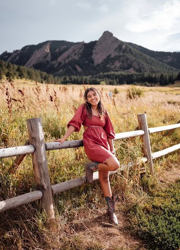 Kavya Kataria, Silver Creek Graduate leaning on the fence and smiling with mountains in the background