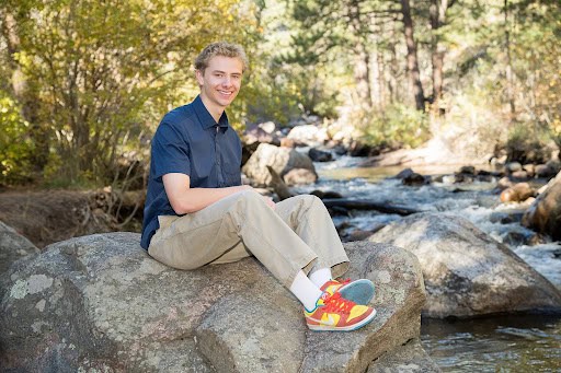 Oliver Welsh, Silver Creek High Graduate sitting on a rock by the creek and smiling
