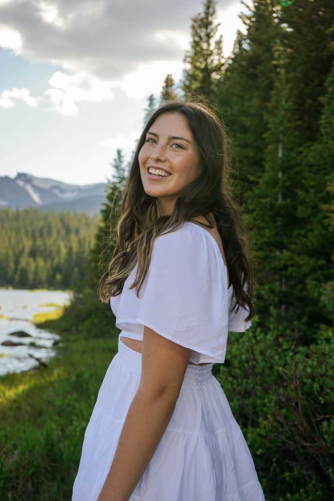 Savannah Pohl standing in front of pine trees next to river smiling at the camera. 