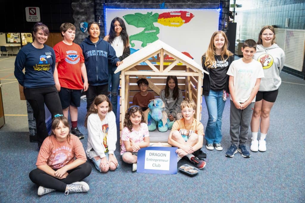 Boys and girls from Sanborn standing around the doghouse they build as they pose for a photo.