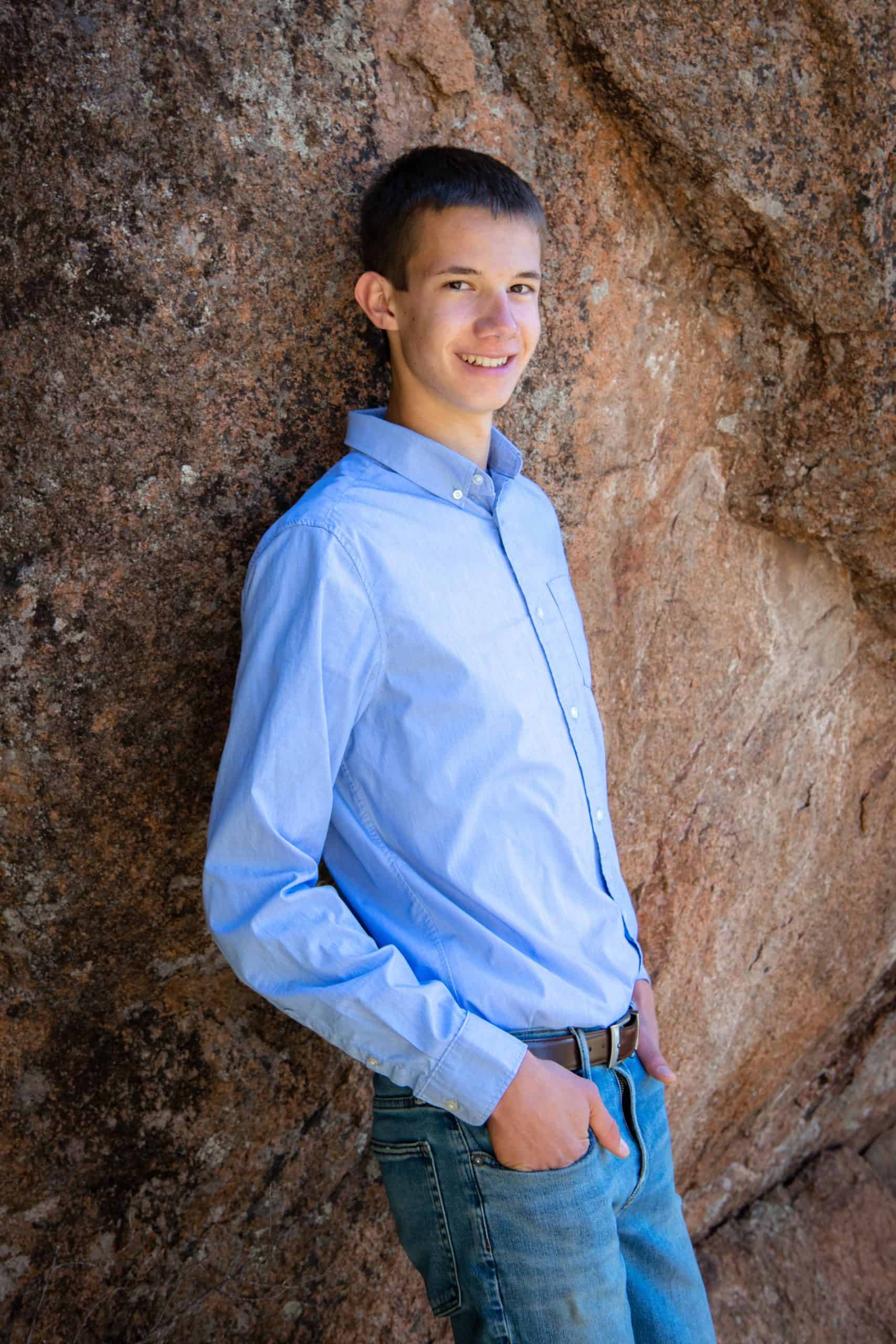 Male student Sage Wynja standing in front of a large wall of rock smiling at the camera. 