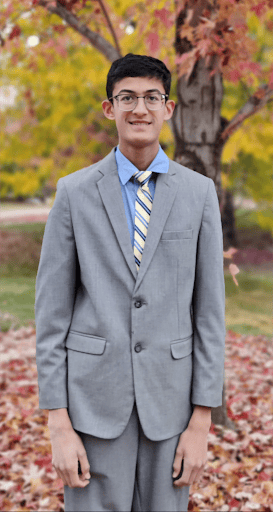 Yash Deshpande wearing a suit standing in front of a tree in the fall. 