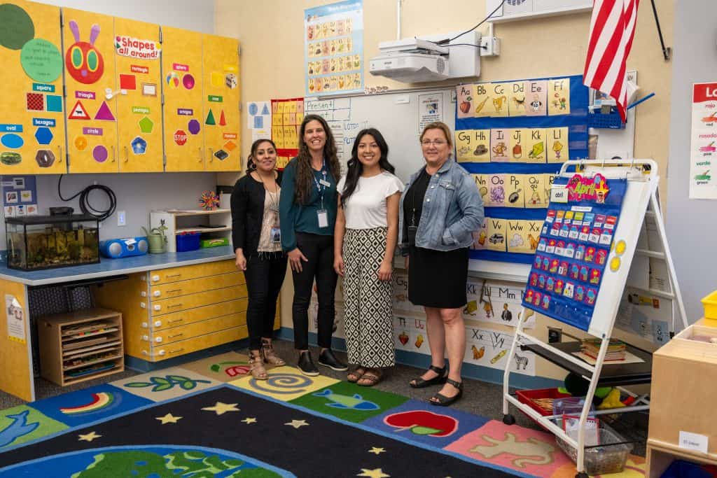 Monica Martinez-Moreno, Nicole Rudman, Ashley Rojas Carbajal, and Paige Gordon smile in a preschool classroom at Spark! Discovery Preschool. 