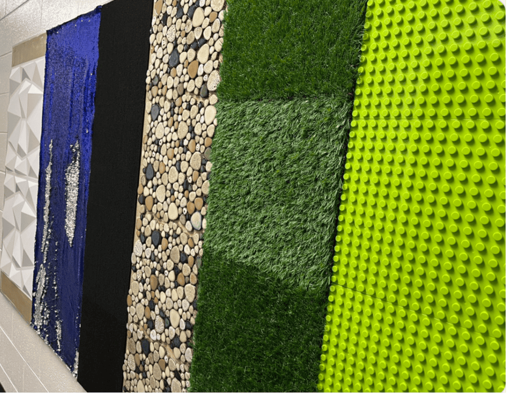 Photo of the sensory wall that shows panels with lego, grass, sequins, felt, rocks