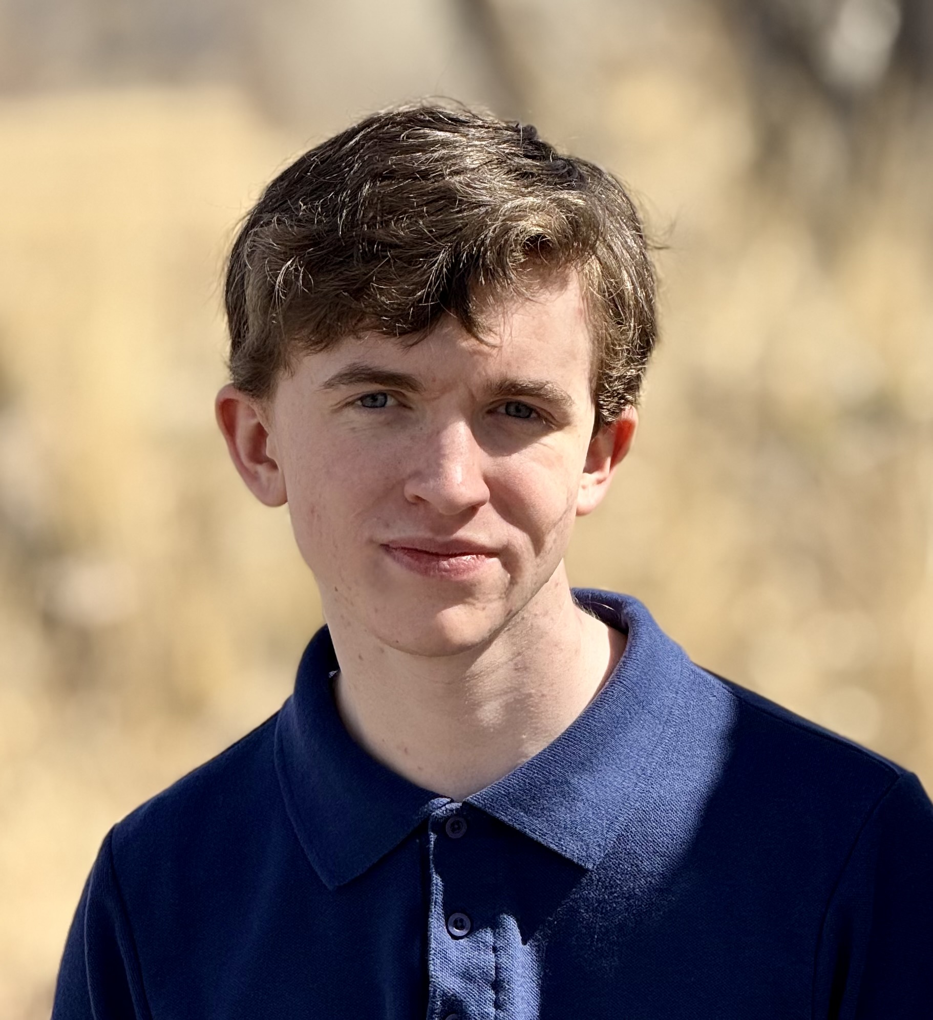 Aidan Dodge, a St. Vrain Virtual High School Senior stands outdoors with a blurred background of tall grass.