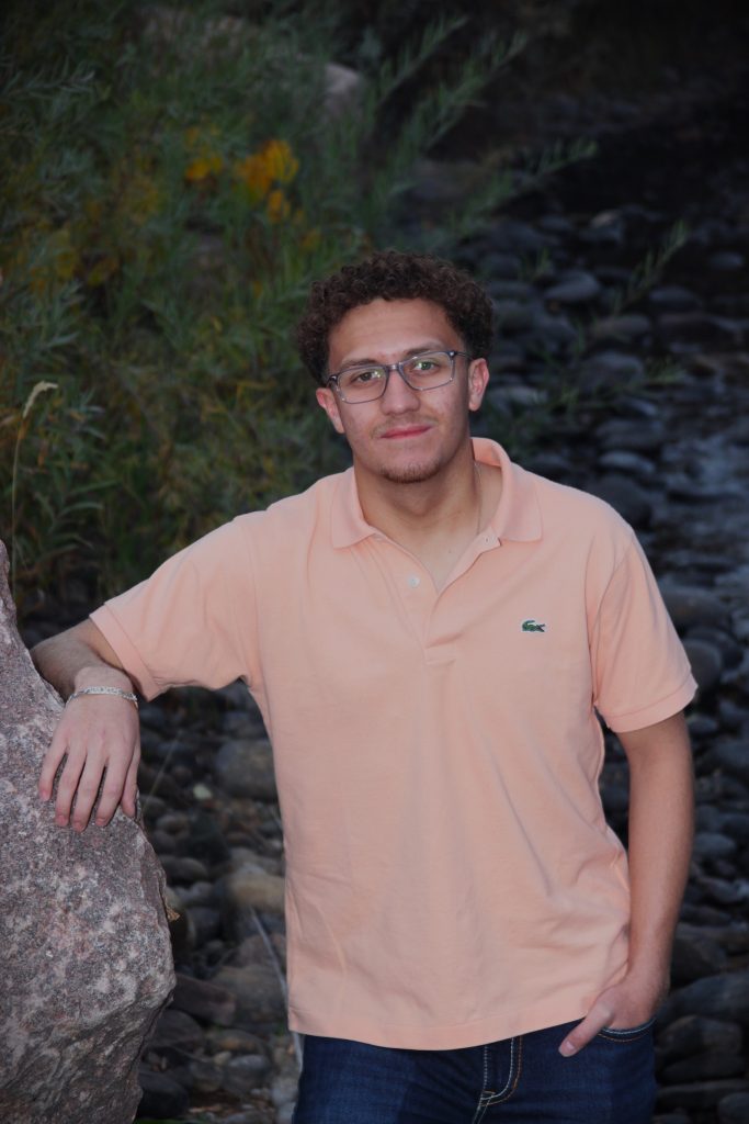 Edgar Neverez Pena, a Skyline High School Senior stands by a rocky stream, with greenery in the background.