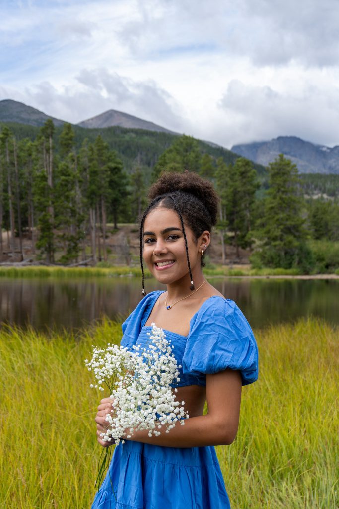 Kaya Fountain, a Frederick High Senior smiles while holding a bouquet of white flowers, with mountains and trees in the background.