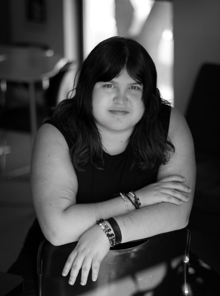 Wylie Leigh, a New Meridian High School Senior sits calmly, resting her arms on a chair, with a softly lit background.