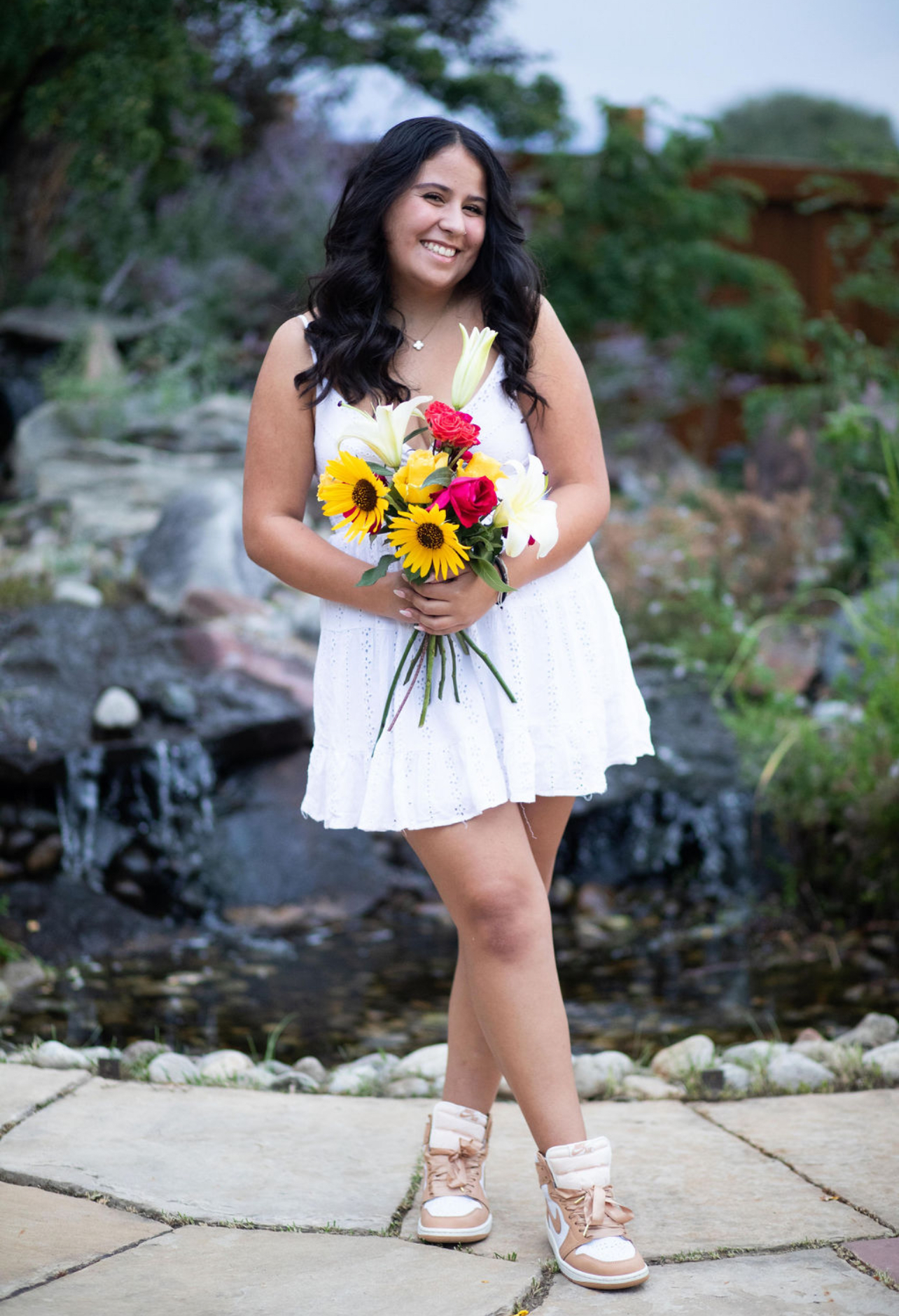 Isabella Palacios, an Eerie High Senior holds a colorful bouquet of flowers by a stone pathway and water feature.