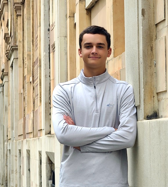 Wyatt Saunders, a Lyons Middle Senior High School Senior leaning against a wall near a building with a historic facade.