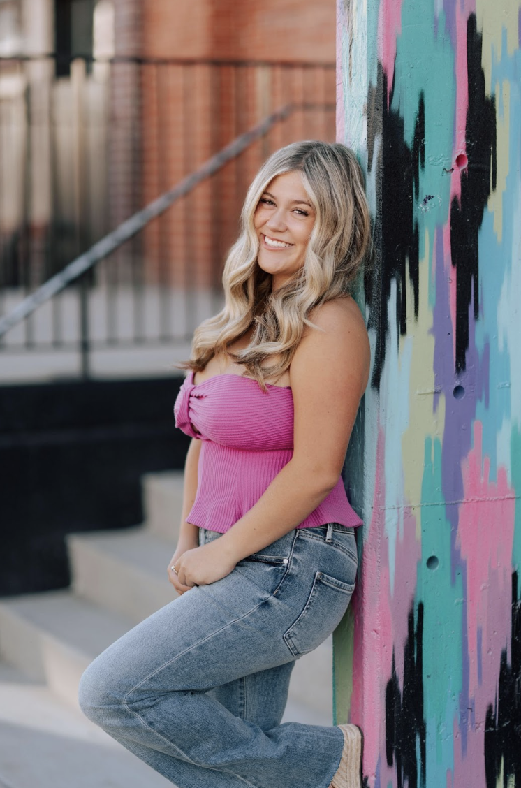 Taylor Morris, a Mead High School Senior leans against a colorful mural while standing on steps.