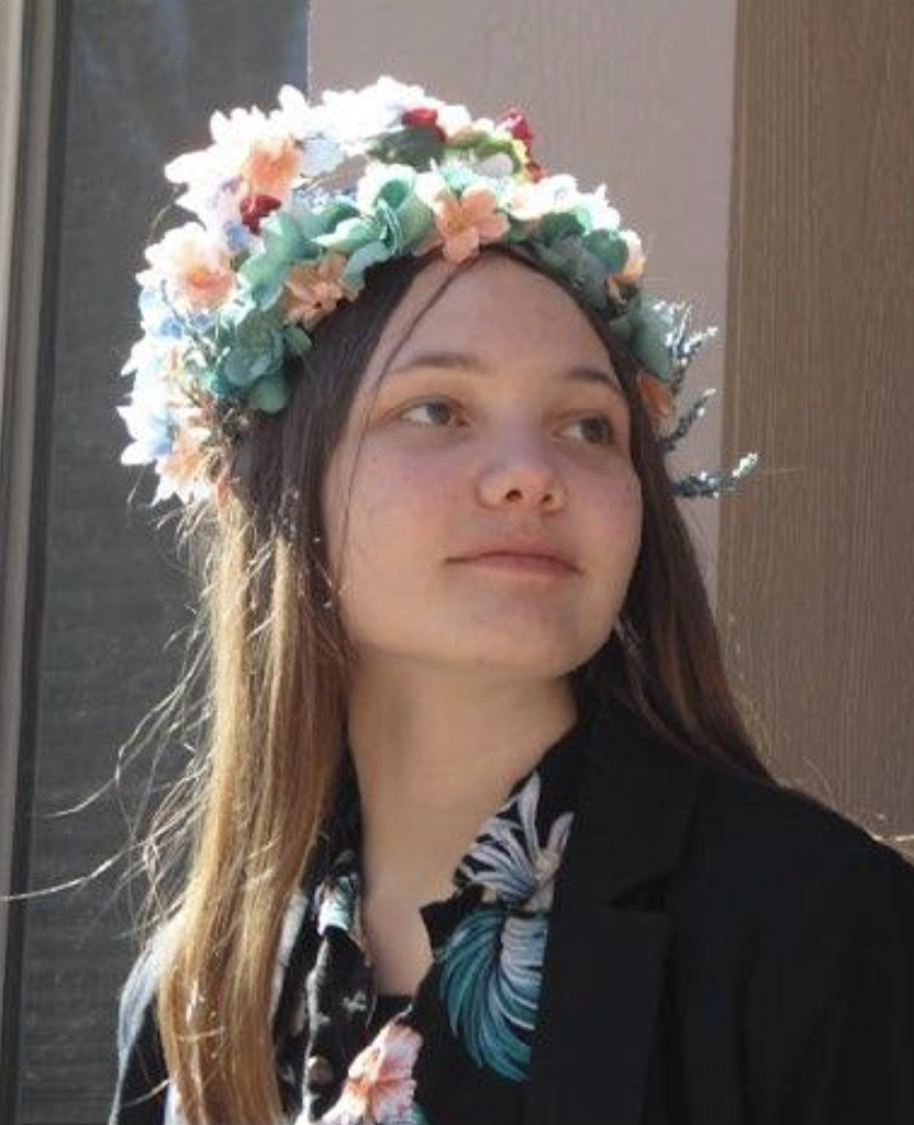 Brynne Geittmann, a Silver Creek High School Senior wears a floral crown and a dark jacket, looking thoughtfully to the side.