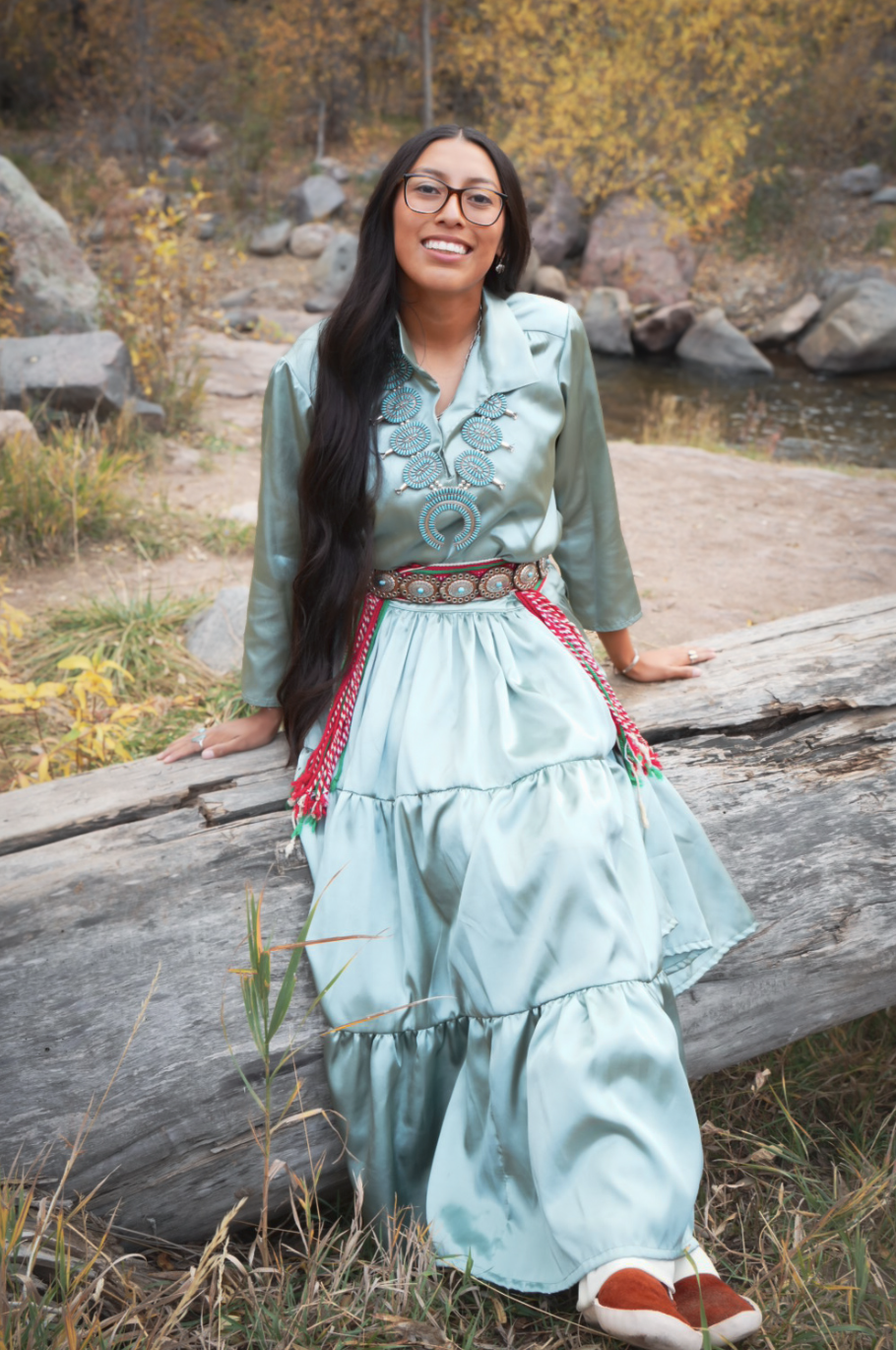 Kianna Butler, a Niwot High School Senior sits on a log near a creek, surrounded by autumn foliage in a serene setting.