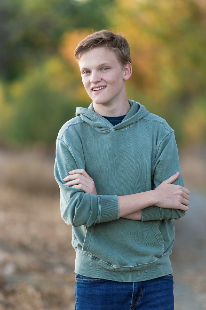 Malcolm Smith, a Niwot High School Senior wearing a green hoodie and jeans, standing outdoors with blurred nature background.