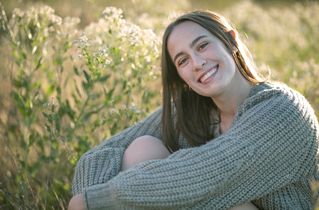 Brooklyn Baum, a Silver Creek senior sits in a field of flowers, bathed in warm, soft sunlight.