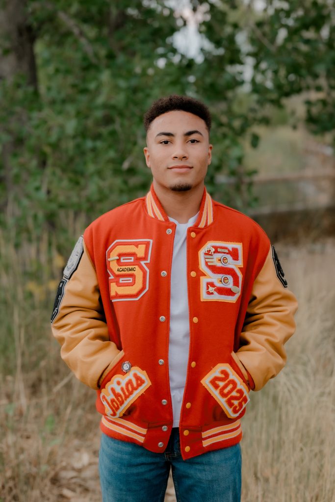 Tobias Pinson, a Skyline High School Senior stands confidently outdoors, surrounded by greenery.