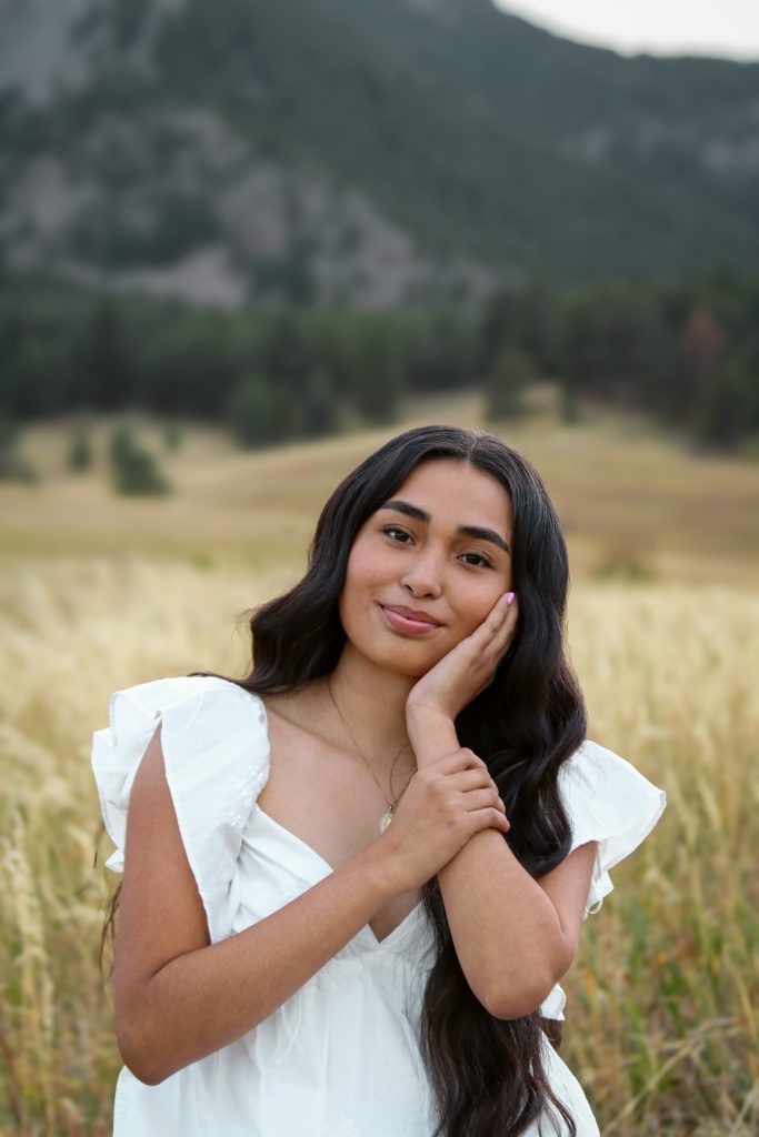 Rocio Uvina Perez, a Longmont High Senior smiling and resting her chin on her hand against a scenic mountain backdrop.