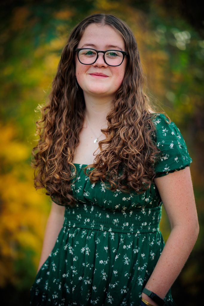 Anya Wieder, a Longmont High Senior stands in front of colorful autumn foliage, wearing a green floral dress.