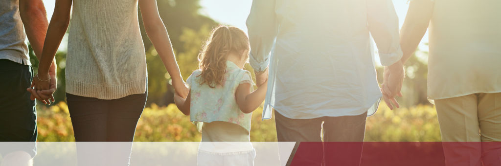 A group of people, including a child, hold hands while walking together in a sunny outdoor setting.