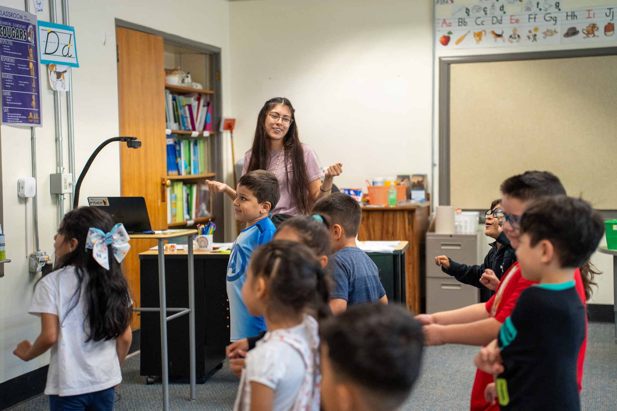 A teacher leads a class of children engaged in a fun activity in a bright, colorful classroom.