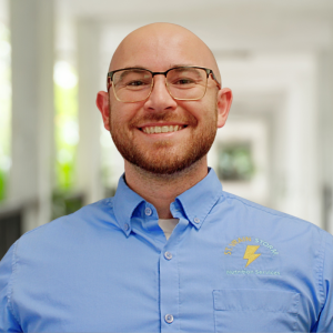 A smiling man with a bald head and beard wears a blue shirt with "Nutrition Services" embroidered on it.