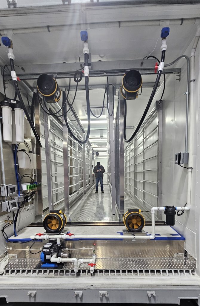 Interior de unas instalaciones con estanterías metálicas, tuberías y una persona de pie en el centro, rodeada de maquinaria.