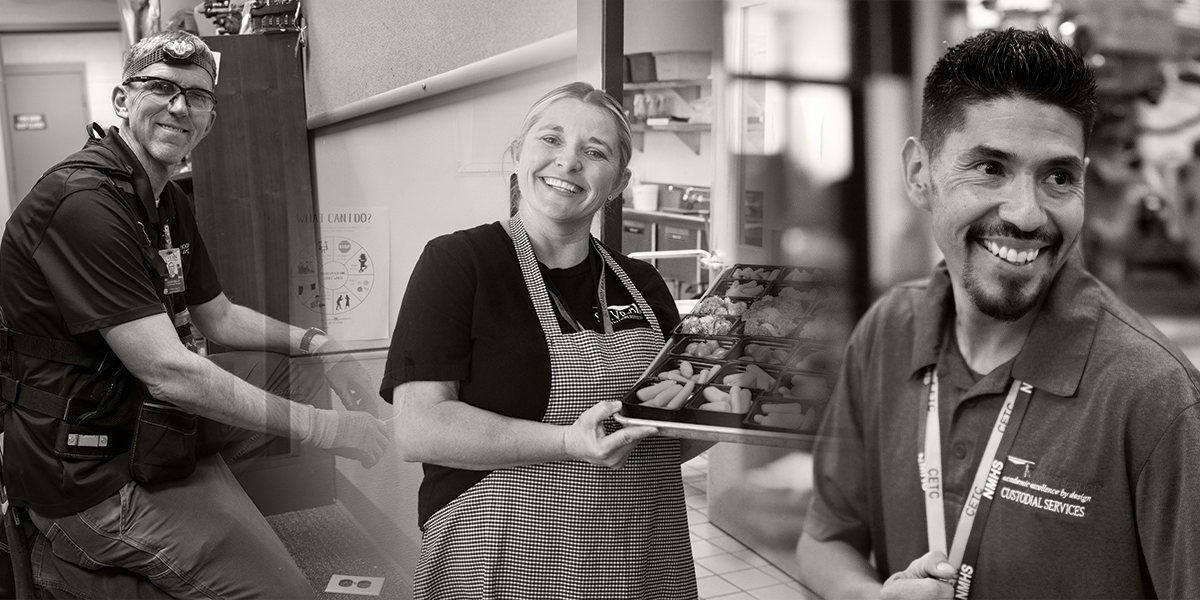 Tres personas sonrientes en una cocina: una con una linterna frontal, otra con bandejas de comida y otra con uniforme de conserje.