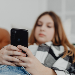 Un joven está tumbado en un sofá, absorto en su teléfono móvil, vestido con una camisa a cuadros.