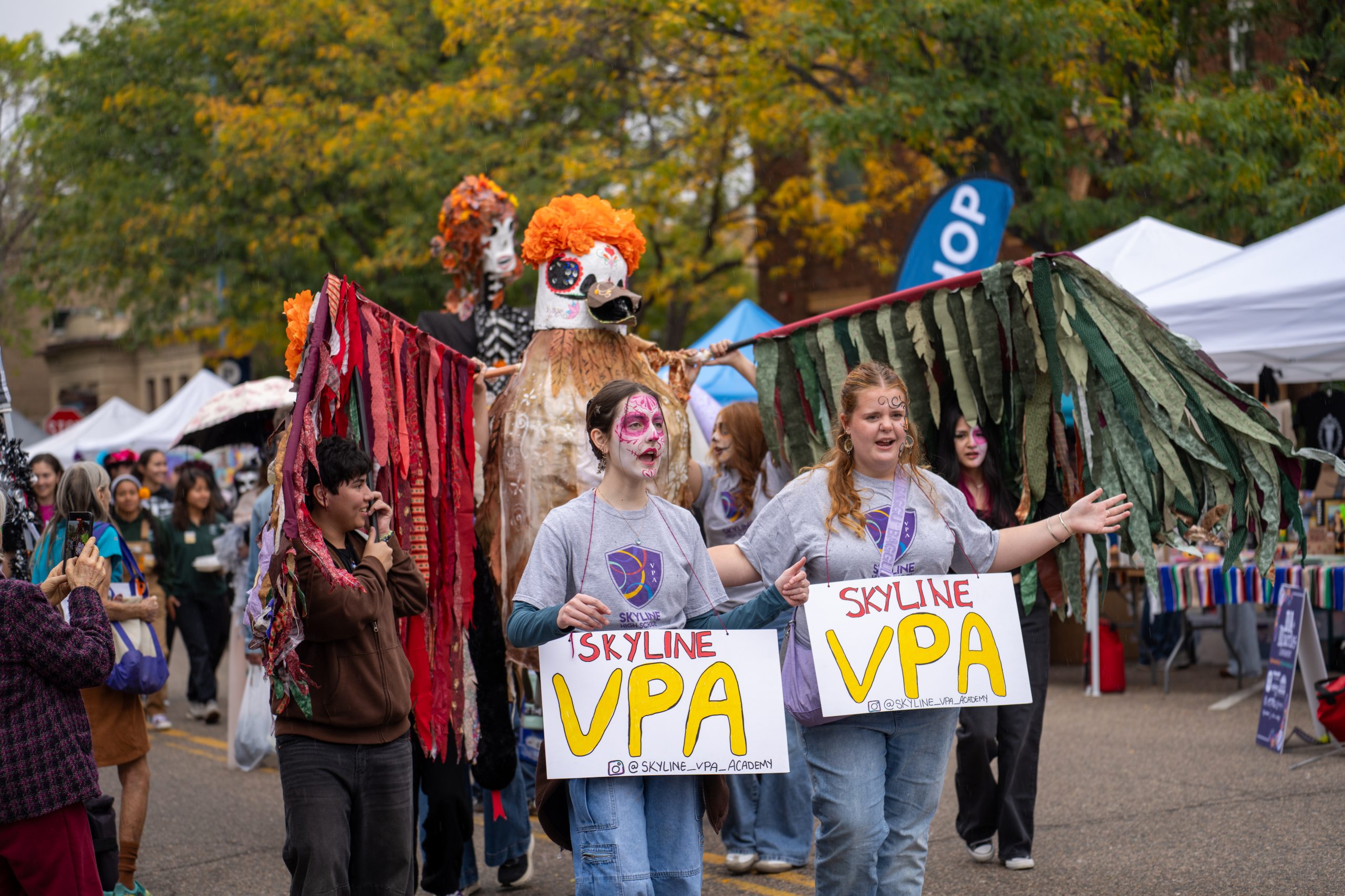 Los participantes, ataviados con trajes de gala, desfilan en un desfile portando carteles con el lema «Skyline VPA» en medio de un ambiente festivo.