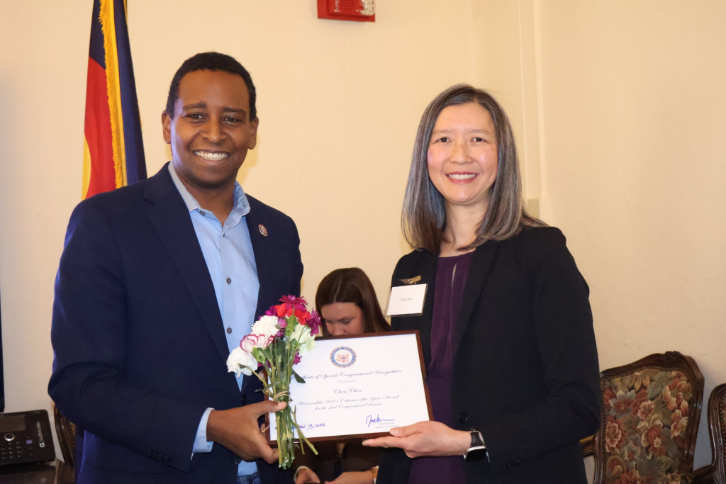 Joe Neguse and Chris Chou smile while holding her Congressional Award for Educator of the Year.