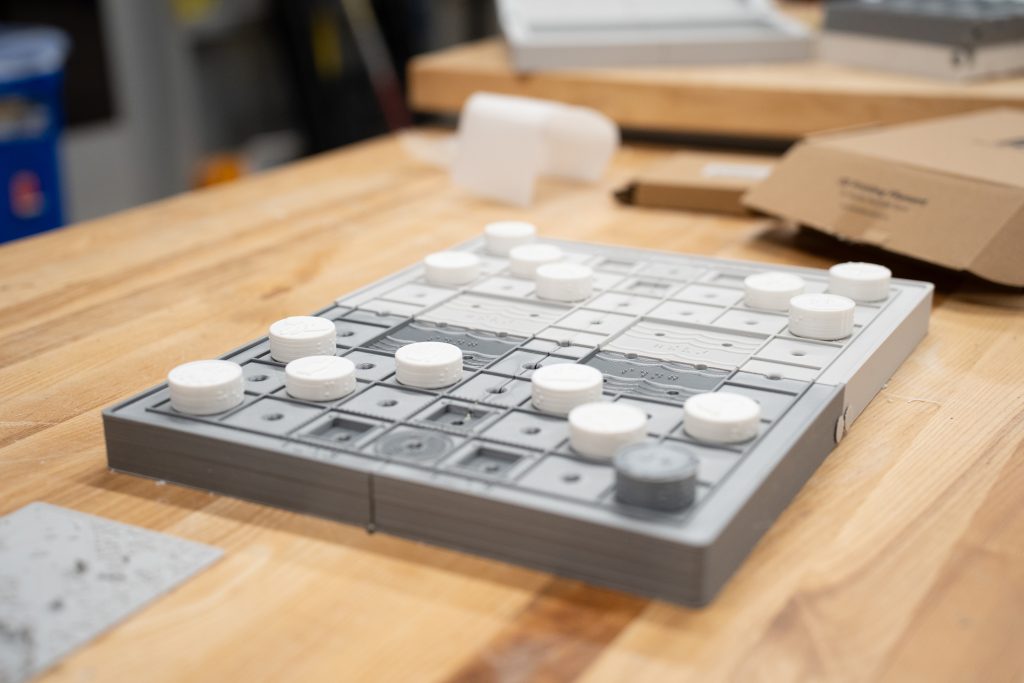 A game board with gray and white pieces arranged on a wooden table, with packaging materials nearby.