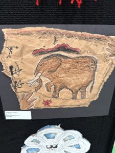 A colorful drawing of an elephant on textured paper, with abstract symbols around it, displayed on a black background.