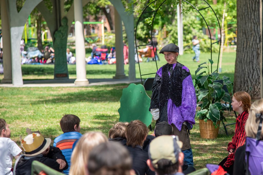 Un niño vestido con un traje morado actúa en el escenario mientras un grupo de niños lo observa en un parque.