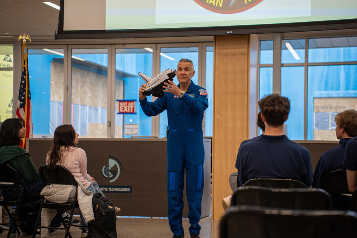 Duane Carey holds a model spaceship while speaking to an audience seated at the Innovation Center.