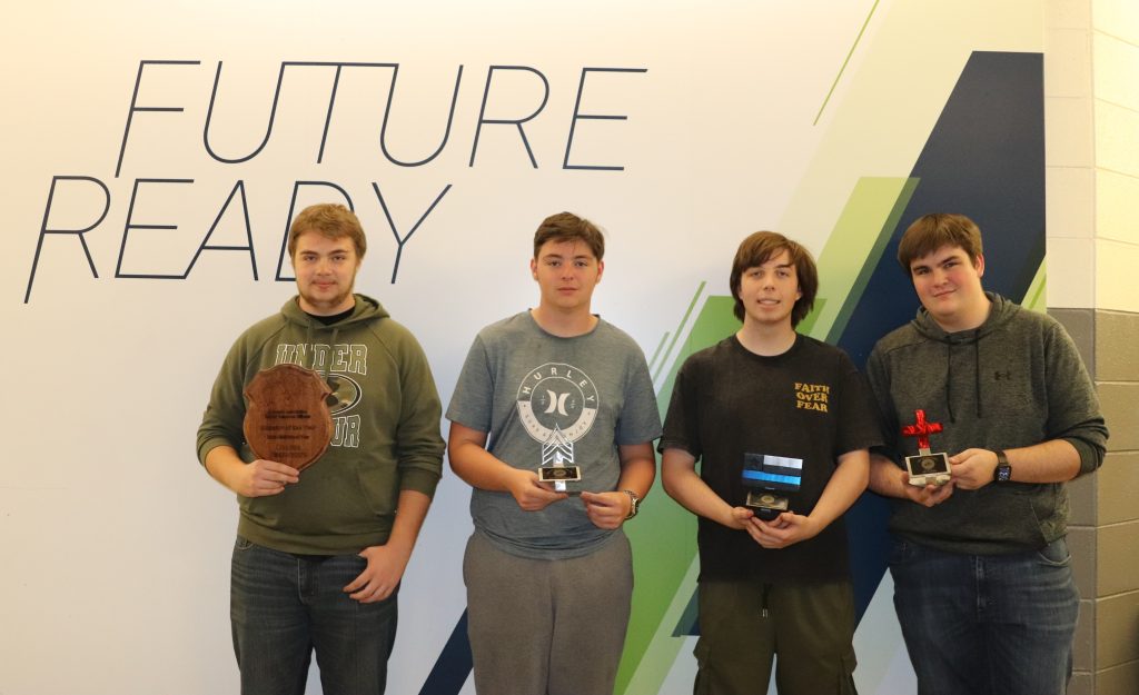 Four students stand together, each holding awards, in front of a wall that says "FUTURE READY."