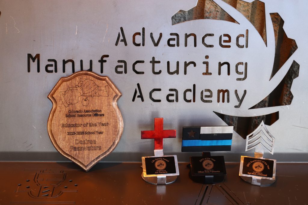 Wooden and metal awards displayed against a metal sign reading "Advanced Manufacturing Academy."