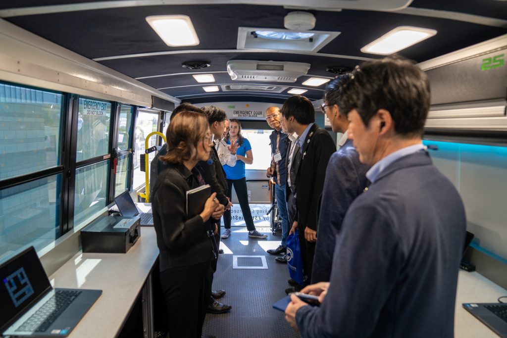 Un grupo de personas en un autobús habla sobre ciberseguridad y formación en inteligencia artificial, con ordenadores portátiles a la vista sobre las mesas.